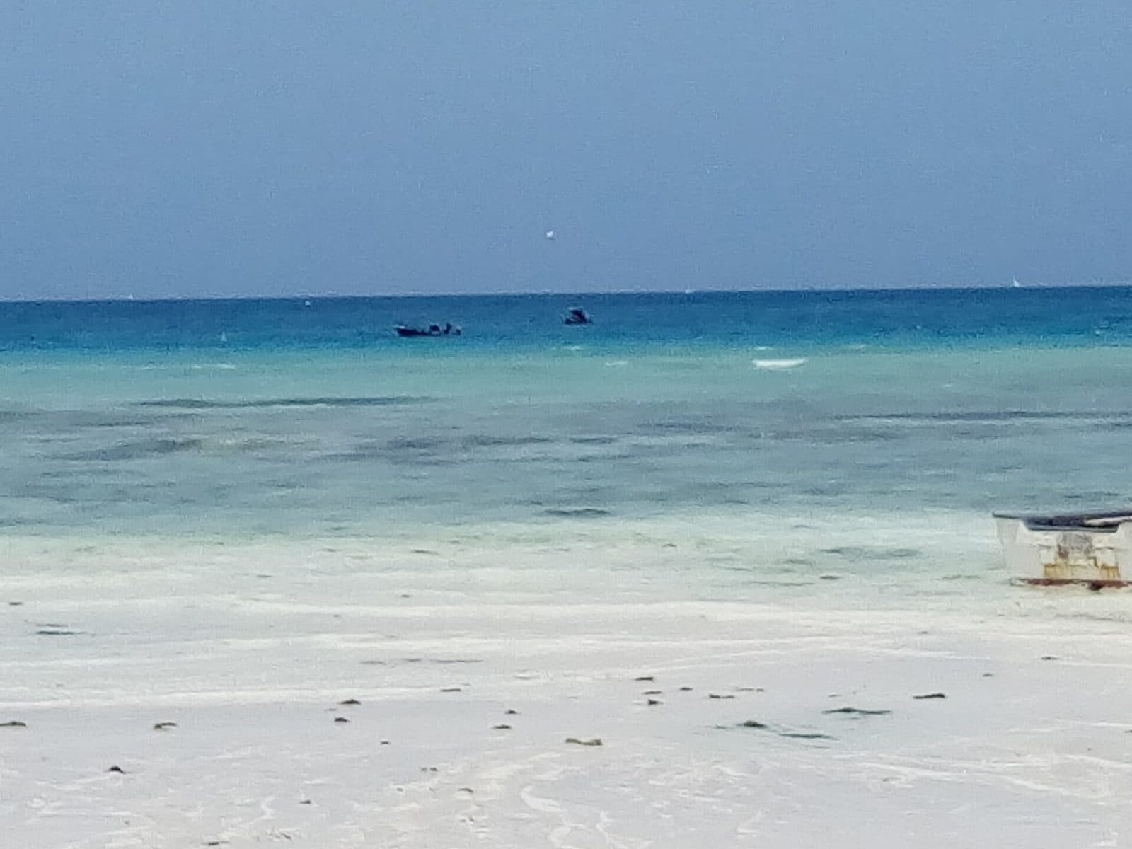 Turquoise water fading over a sandbar at Nungwi beach, with fishing boats on the horizon